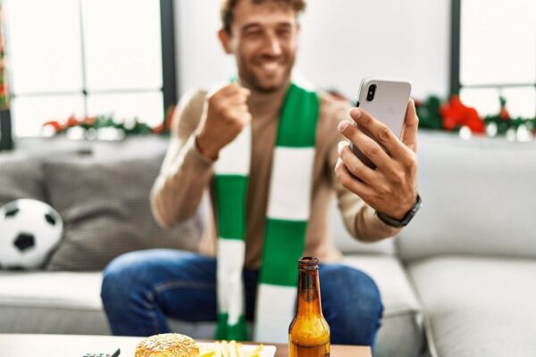muskarac sa salom oko vrata i telefonom u ruci prati sportsku utakmicu